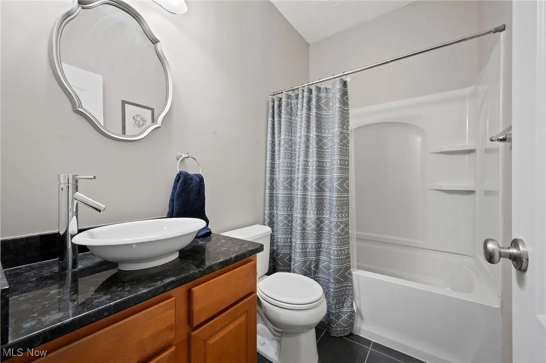 Bathroom featuring vanity, shower / bathtub combination with curtain, and dark tile patterned floors