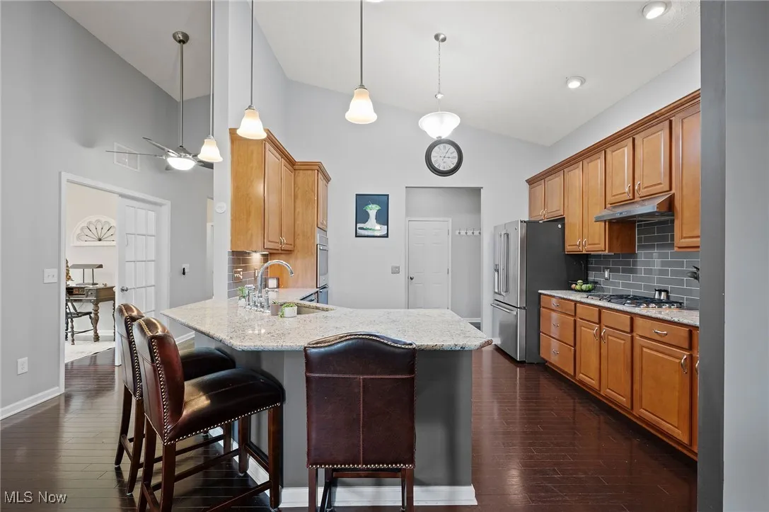 Kitchen featuring backsplash, brown cabinetry, a peninsula, decorative light fixtures, and high vaulted ceiling