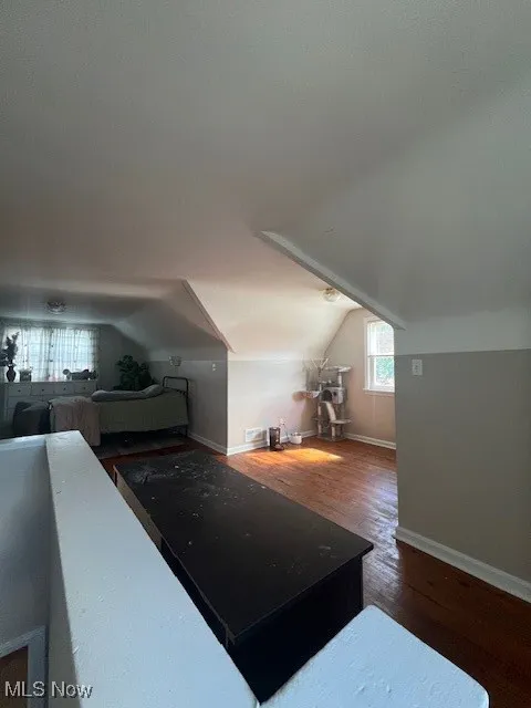 Additional living space with dark wood-style flooring and vaulted ceiling