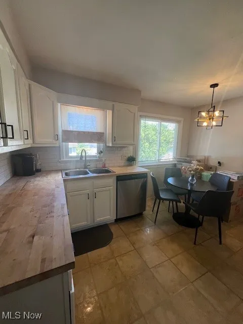 Kitchen featuring white cabinets, decorative light fixtures, stainless steel dishwasher, tasteful backsplash, and wooden counters