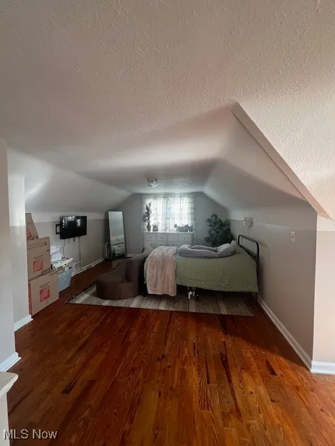 Bedroom with wood finished floors, lofted ceiling, and a textured ceiling