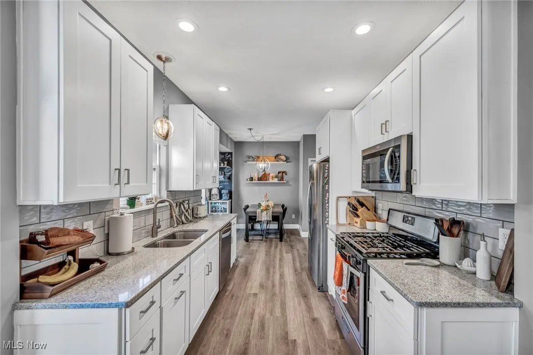 Kitchen featuring stainless steel appliances, tasteful backsplash, light stone counters, white cabinets, and recessed lighting