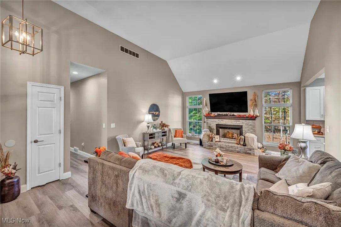 Living area featuring wood finished floors, high vaulted ceiling, a stone fireplace, and recessed lighting