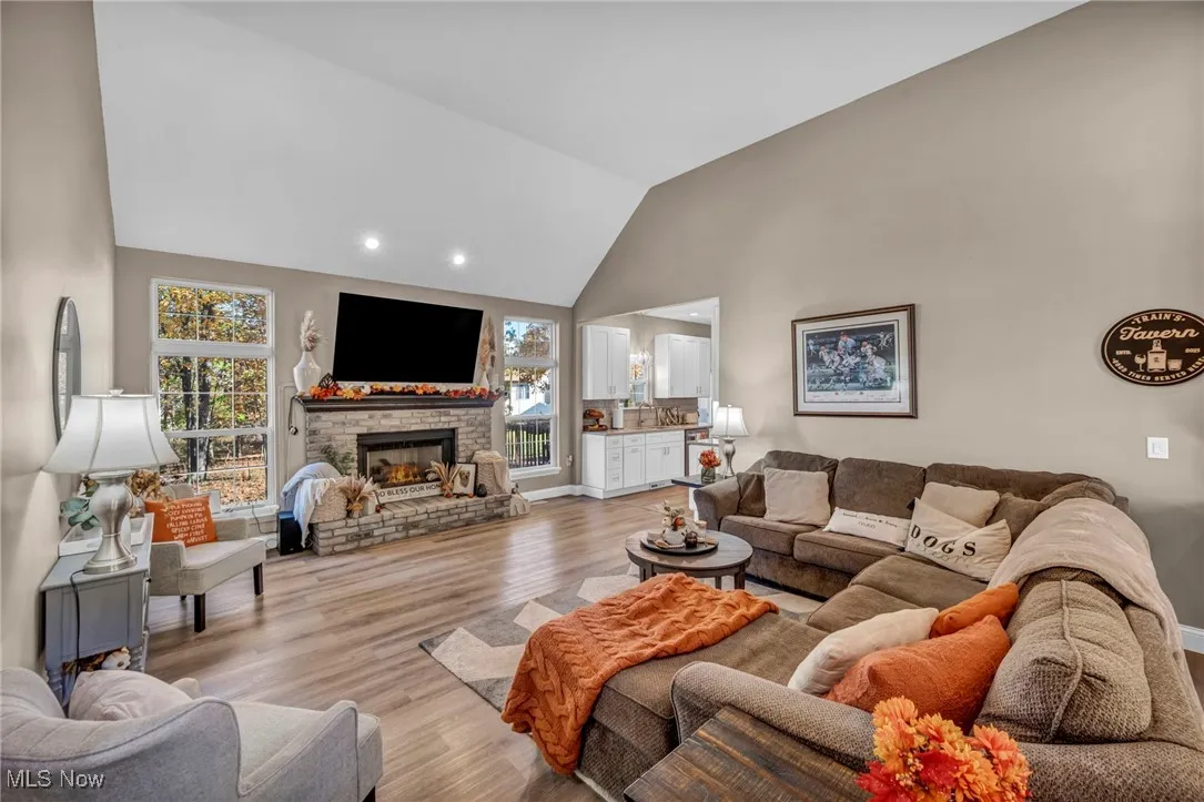 Living area with high vaulted ceiling, light wood-type flooring, a fireplace, and recessed lighting