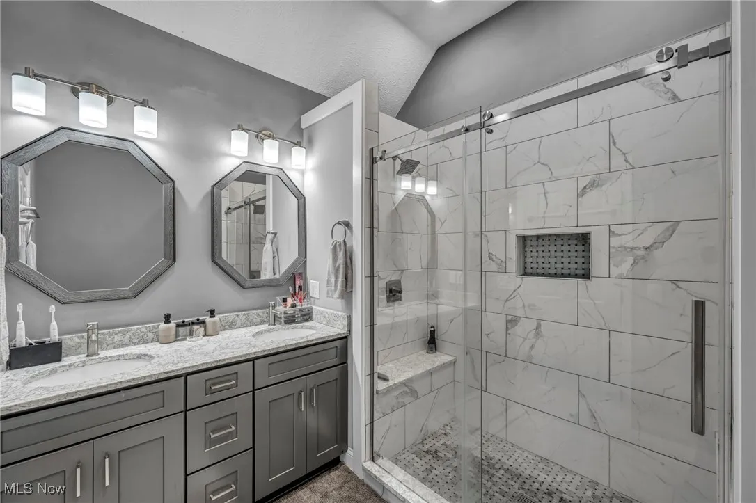 Bathroom with double vanity, a stall shower, and lofted ceiling