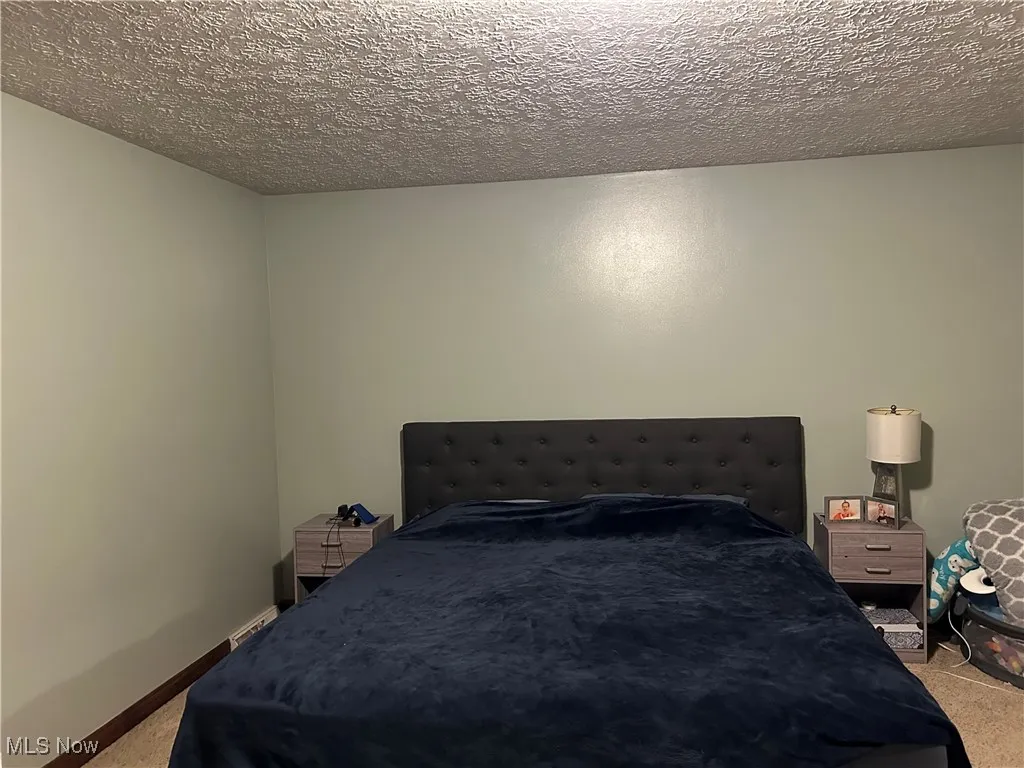 Carpeted bedroom with a textured ceiling and baseboards