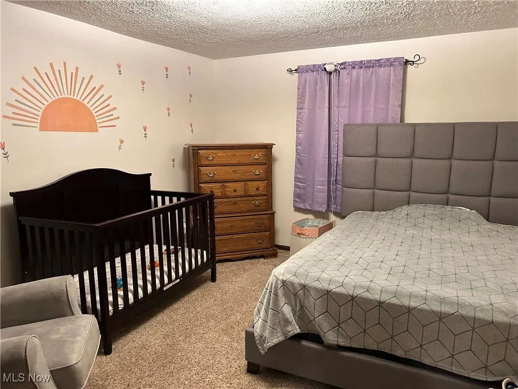 Bedroom with a textured ceiling, light colored carpet, and a nursery area