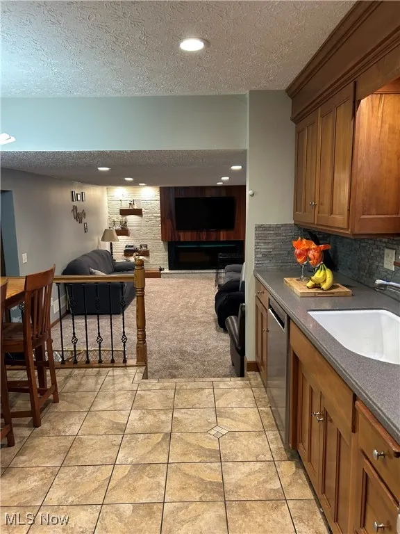 Kitchen with a textured ceiling, open floor plan, brown cabinetry, dishwasher, and recessed lighting