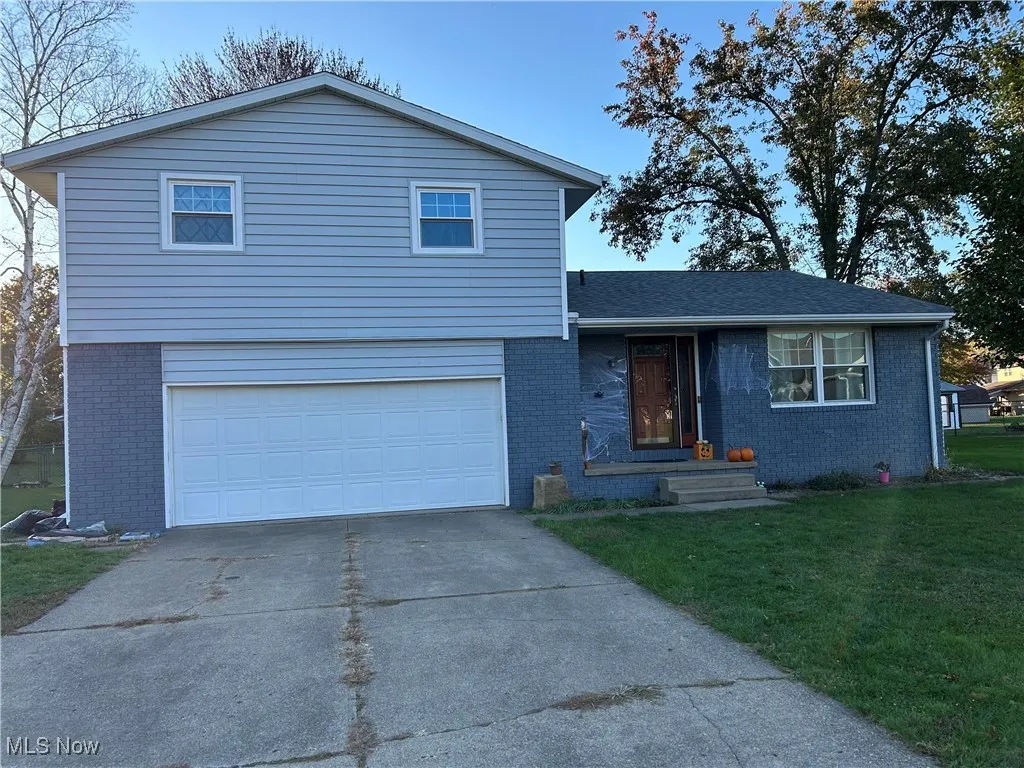 Tri-level home with a front yard, brick siding, driveway, a garage, and roof with shingles