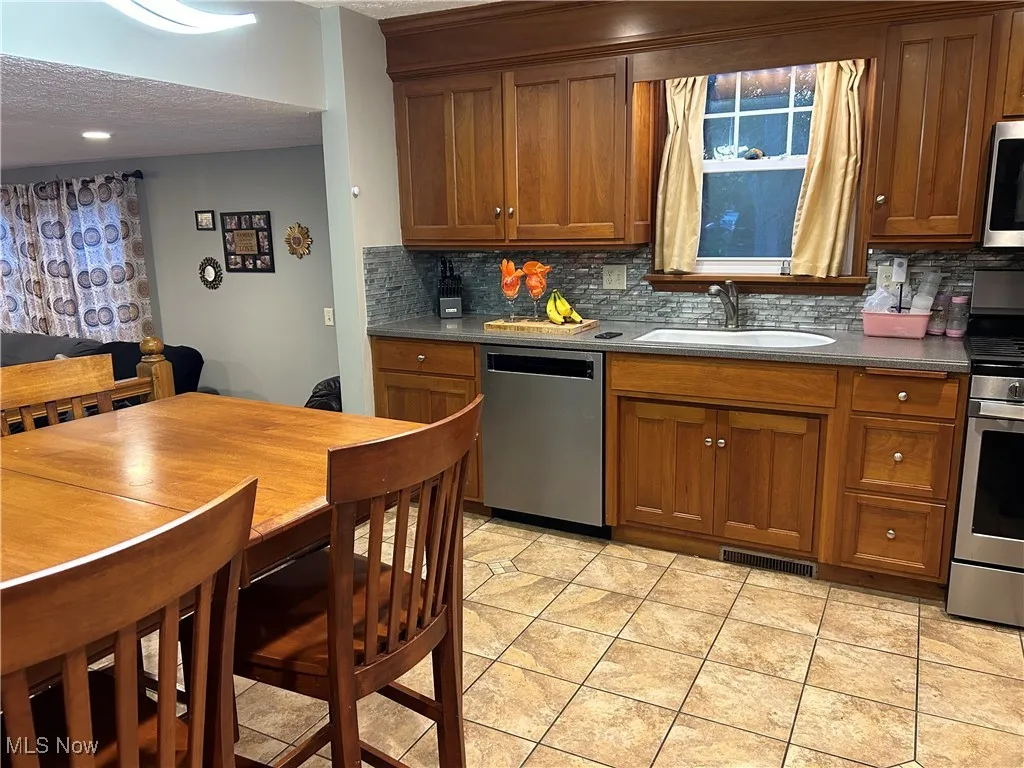 Kitchen featuring brown cabinets, tasteful backsplash, stainless steel appliances, a textured ceiling, and light tile patterned floors
