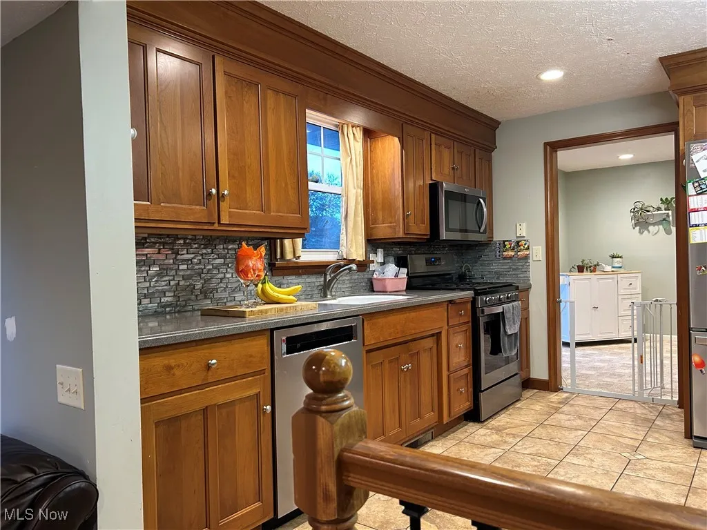 Kitchen featuring brown cabinets, appliances with stainless steel finishes, light tile patterned floors, decorative backsplash, and a textured ceiling