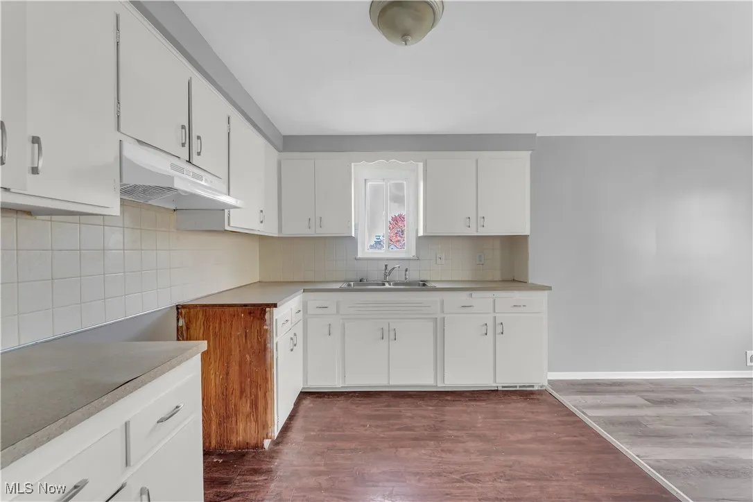 Kitchen featuring dark wood-style flooring, white cabinets, under cabinet range hood, light countertops, and backsplash