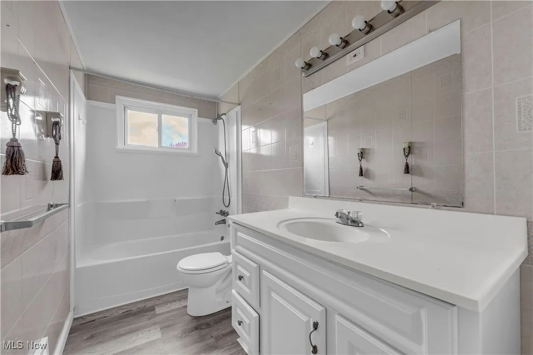 Bathroom with tile walls, vanity, washtub / shower combination, and light wood-style floors