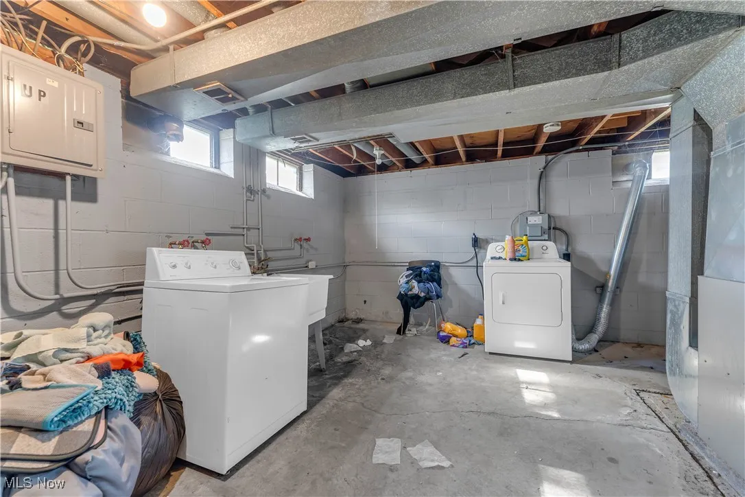 Laundry room featuring electric panel, unfinished concrete floors, heating unit, and washer and dryer