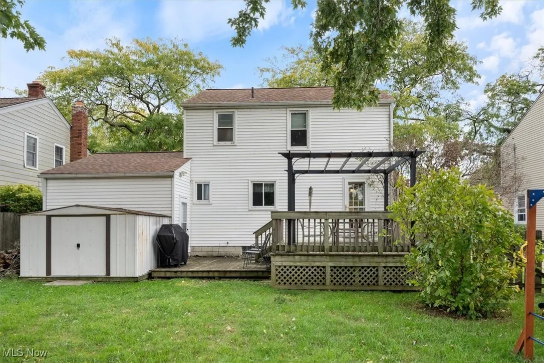 Rear view of house with a shed, a wooden deck, a lawn, and a pergola