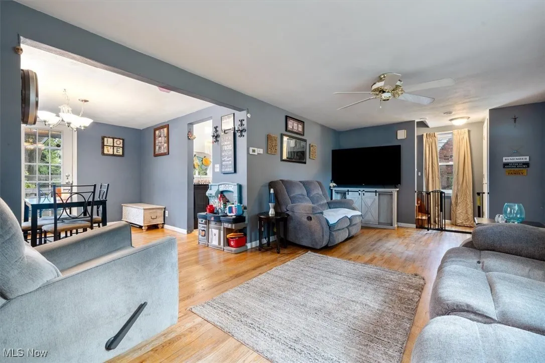Living area with wood finished floors, plenty of natural light, a chandelier, and ceiling fan