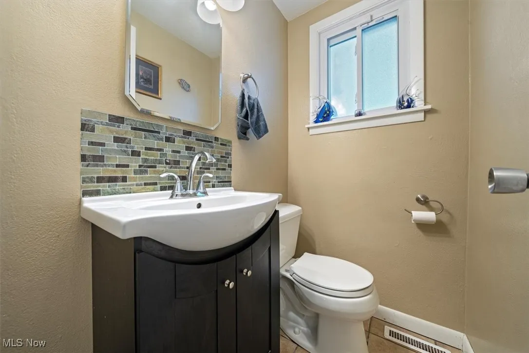 Half bathroom with a textured wall, decorative backsplash, vanity, and tile patterned flooring