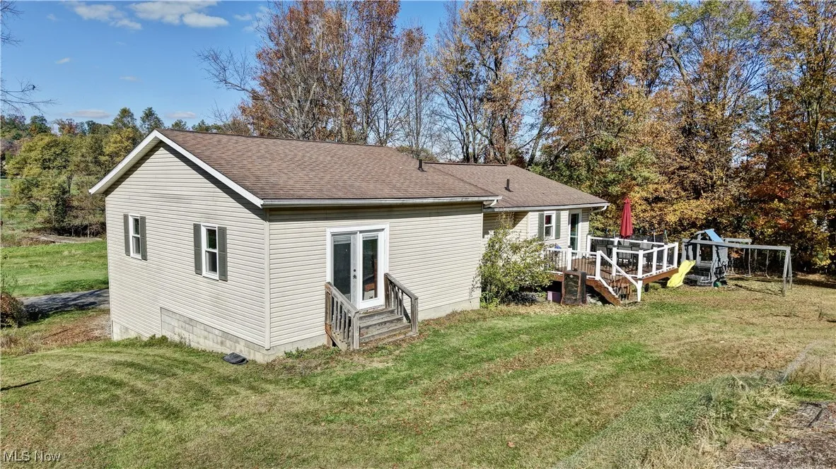 Rear view of property with a shingled roof, a lawn, a wooden deck, and entry steps