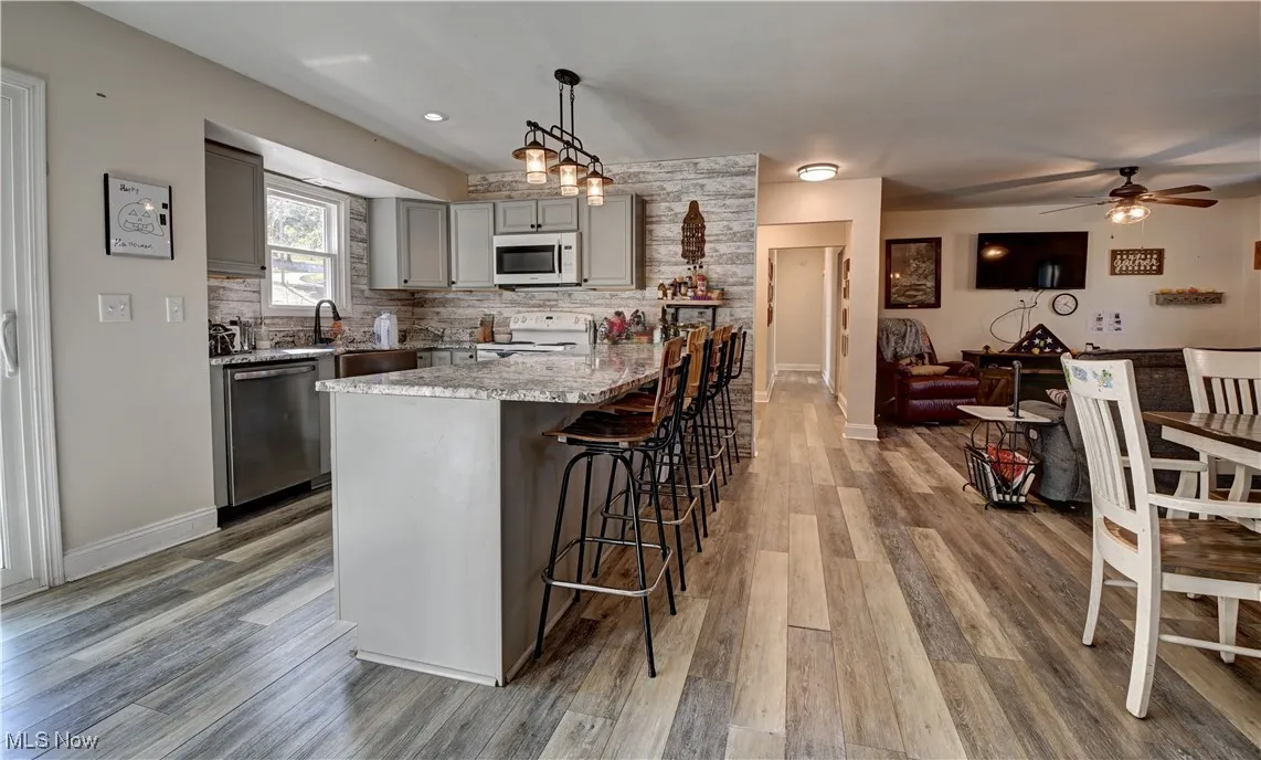 Kitchen with gray cabinets, tasteful backsplash, a kitchen bar, white appliances, and decorative light fixtures