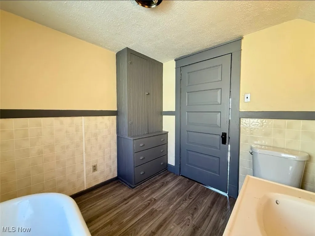 FH-2ND FL FULL Bathroom featuring tile walls, a bathtub, a wainscoted wall, dark wood-style flooring, and a textured ceiling