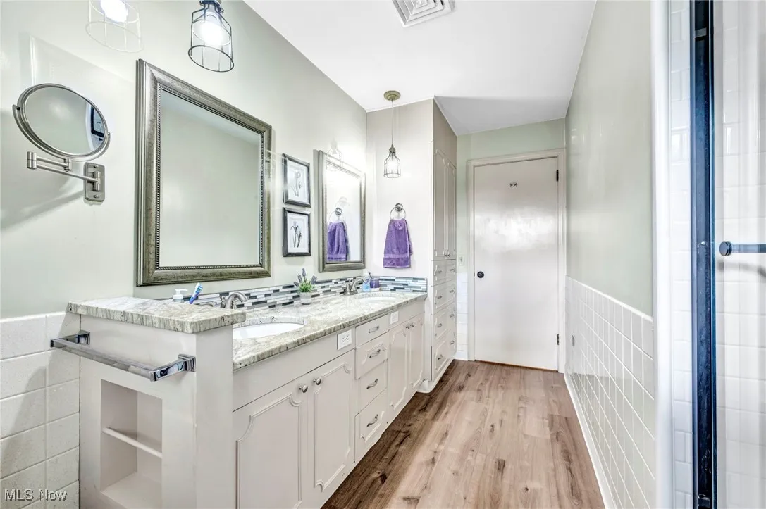 Full bathroom with tile walls, a wainscoted wall, light wood finished floors, double vanity, and an enclosed shower