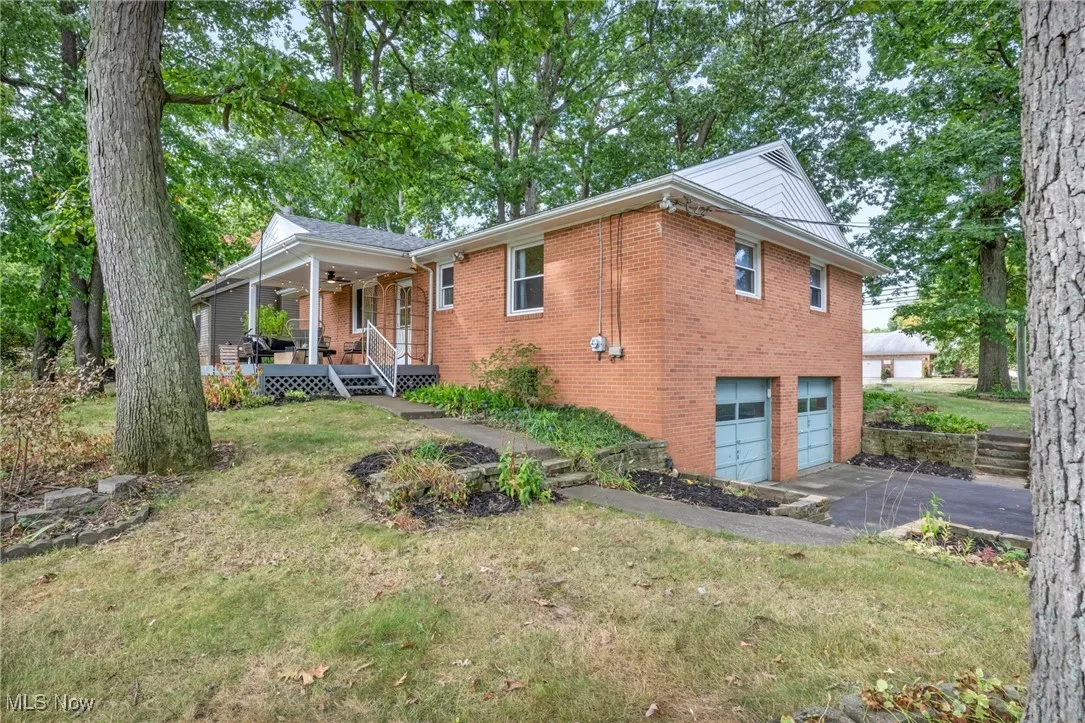 View of side of property featuring a lawn, brick siding, an attached garage, a porch, and asphalt driveway
