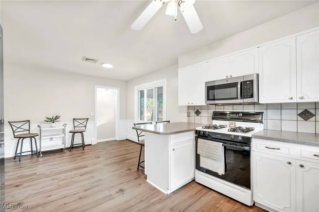 Kitchen with gas range oven, a peninsula, stainless steel microwave, a breakfast bar area, and white cabinetry