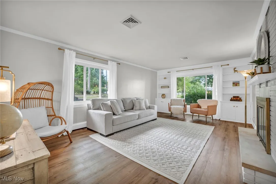 Living area featuring ornamental molding, a glass covered fireplace, wood finished floors, and built in features