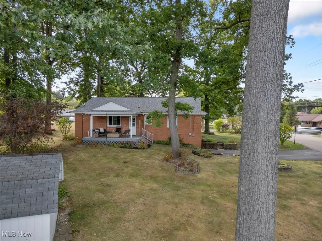 View of front of property with a front lawn, a deck, a shingled roof, and brick siding
