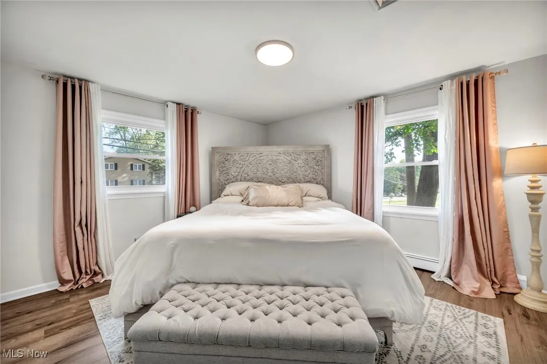 Bedroom featuring wood finished floors, multiple windows, and baseboard heating