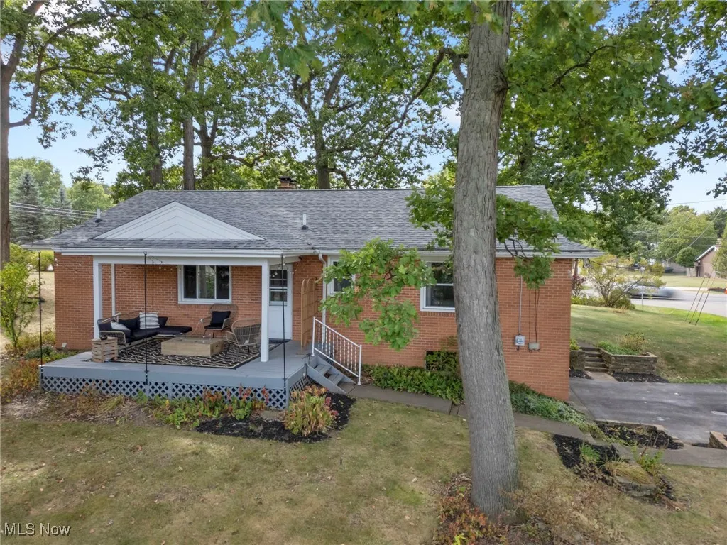 View of front of house featuring a front lawn, brick siding, a chimney, roof with shingles, and a deck