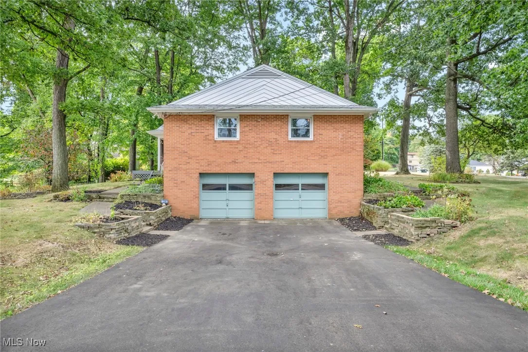 View of side of home featuring brick siding, a lawn, driveway, and a metal roof