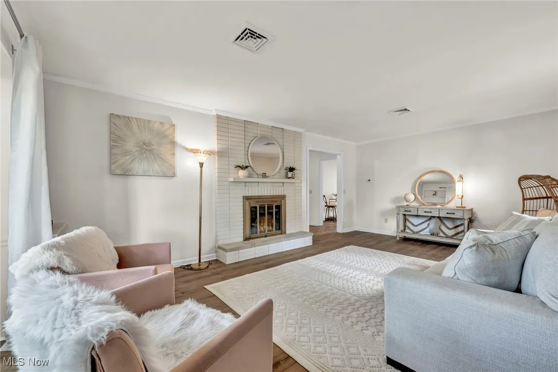Living room featuring wood finished floors, crown molding, and a brick fireplace