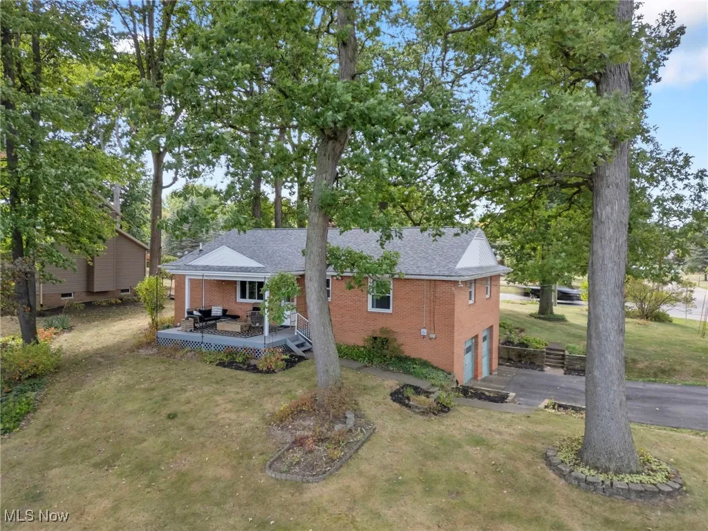 Rear view of house with brick siding, a wooden deck, a garage, a lawn, and asphalt driveway