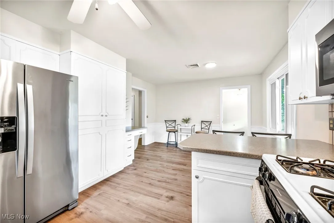 Kitchen featuring appliances with stainless steel finishes, a peninsula, white cabinetry, light wood-style floors, and a wainscoted wall