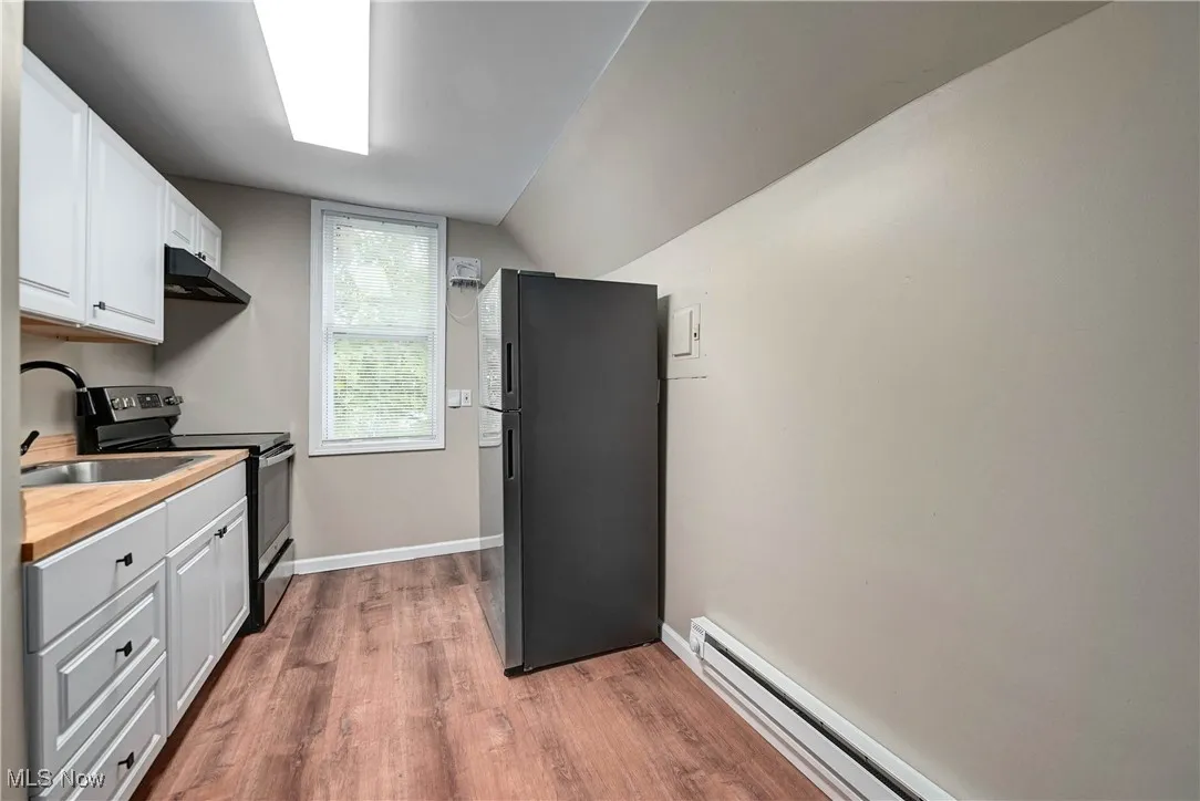 Kitchen featuring a baseboard radiator, white cabinetry, freestanding refrigerator, electric range, and dark wood finished floors