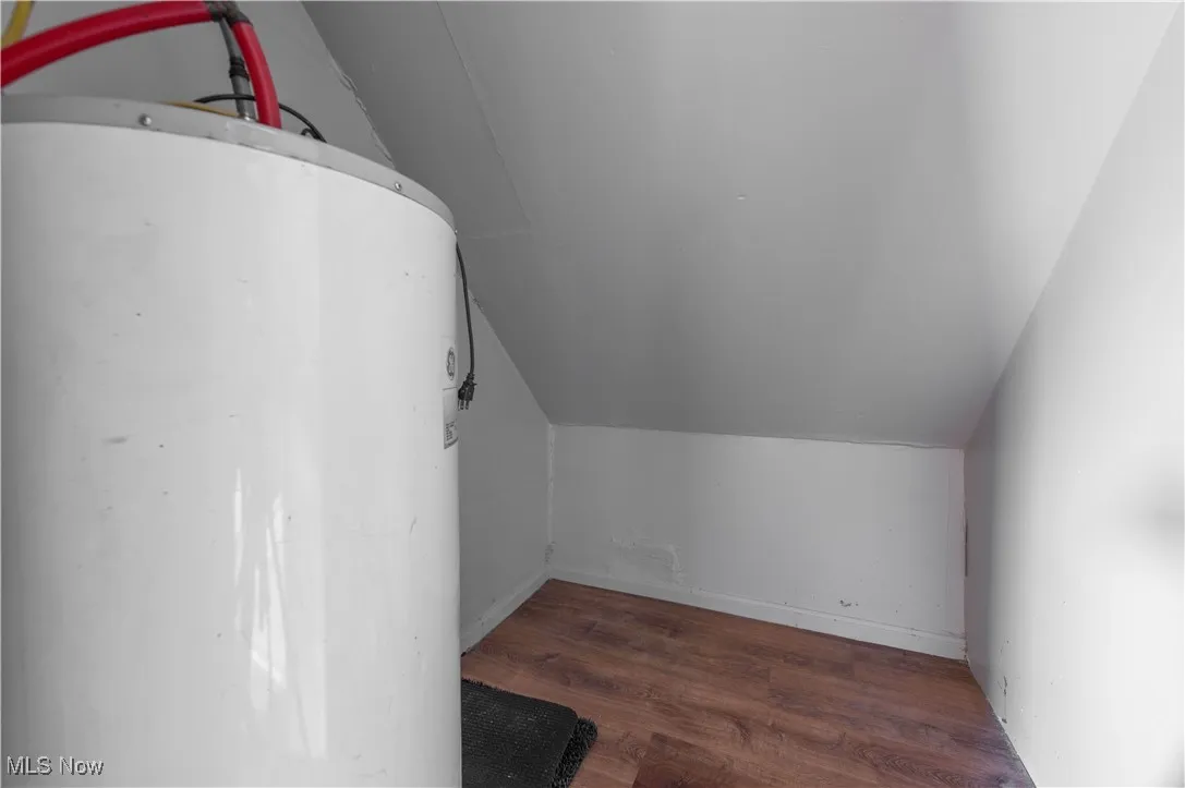 Bonus room with water heater, dark wood finished floors, and vaulted ceiling