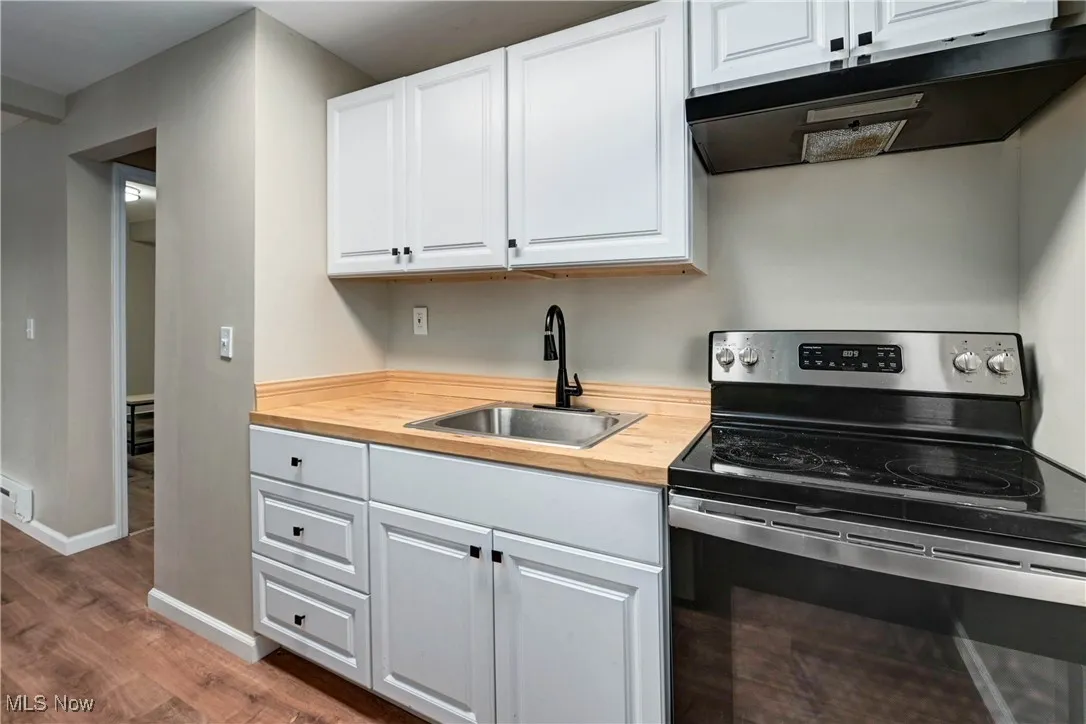 Kitchen with stainless steel range with electric cooktop, under cabinet range hood, white cabinets, dark wood-style flooring, and wooden counters