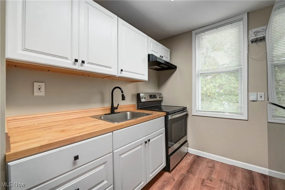 Kitchen featuring electric range, white cabinets, dark wood-style floors, and under cabinet range hood