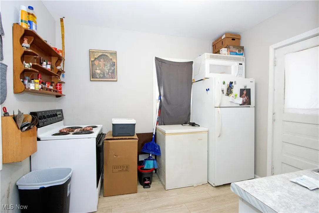 Kitchen with white appliances, open shelves, light wood-style floors, and light countertops
