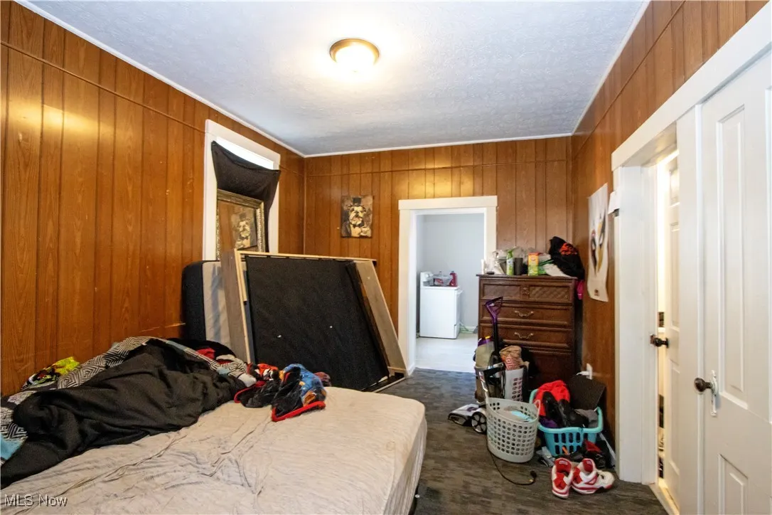 Bedroom featuring wooden walls, dark colored carpet, and washer / clothes dryer