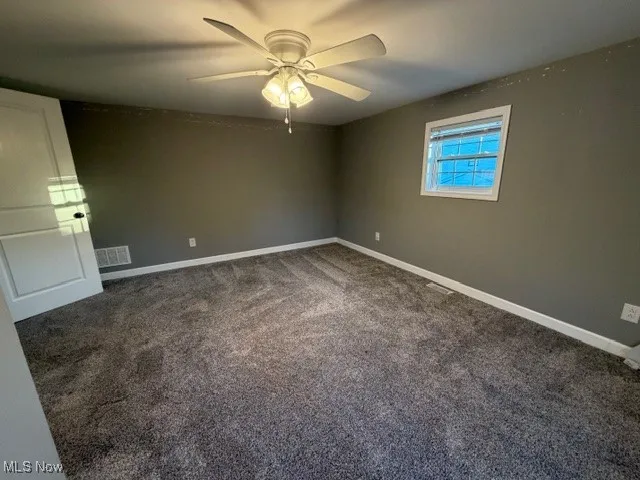 Empty room with dark carpet and ceiling fan