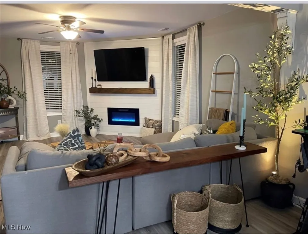 Living area with wood finished floors, a large fireplace, and ceiling fan