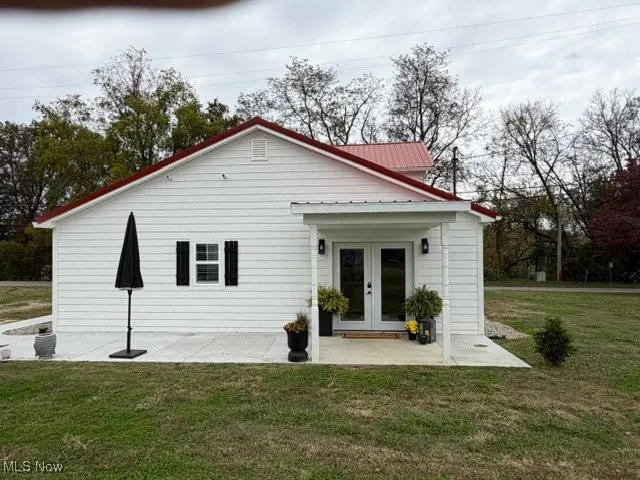 Back of property with a lawn, french doors, and a metal roof