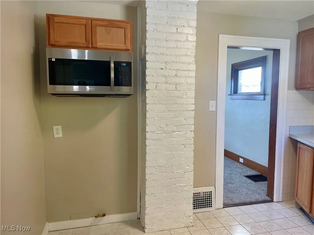 Kitchen with brown cabinets, light tile patterned floors, stainless steel microwave, and light countertops