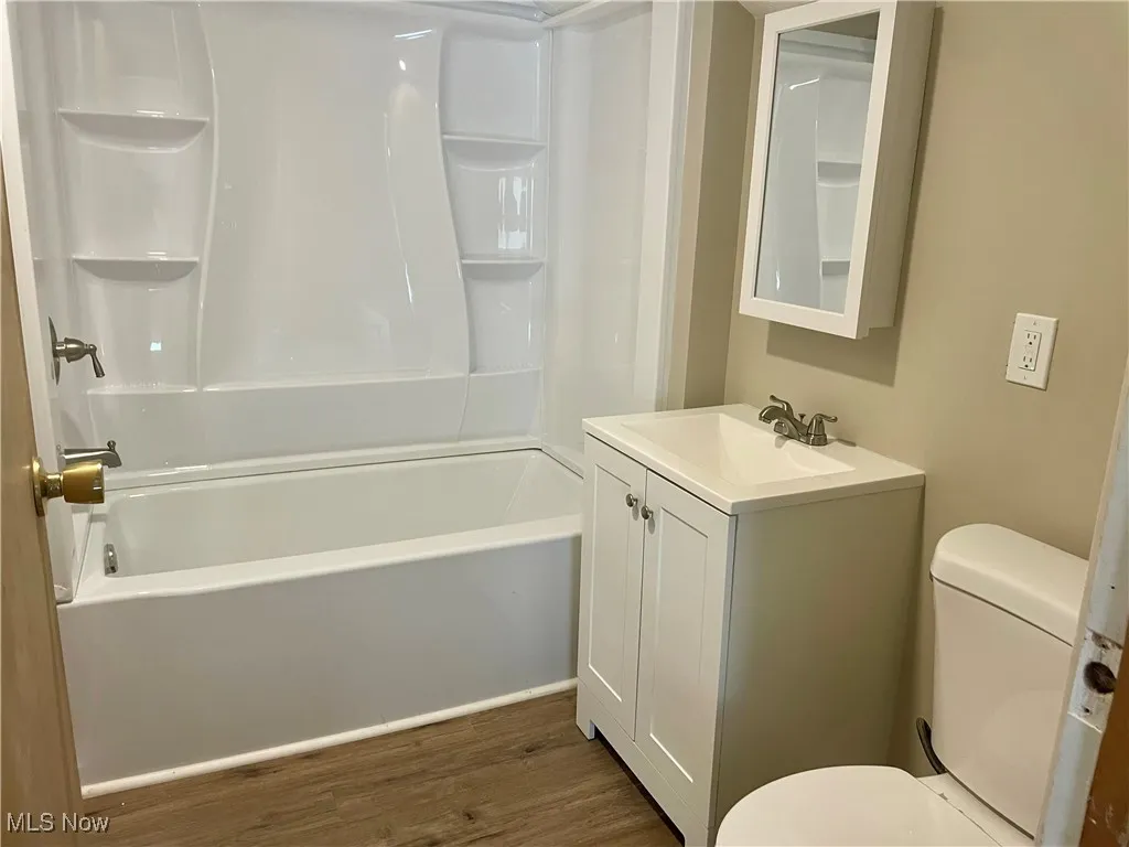 Full bath with dark wood-type flooring, shower / bath combination, and vanity