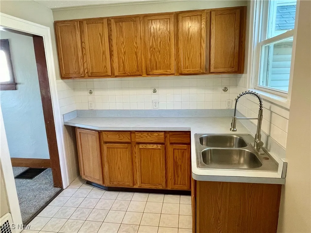 Kitchen featuring brown cabinetry, light countertops, light tile patterned flooring, and tasteful backsplash
