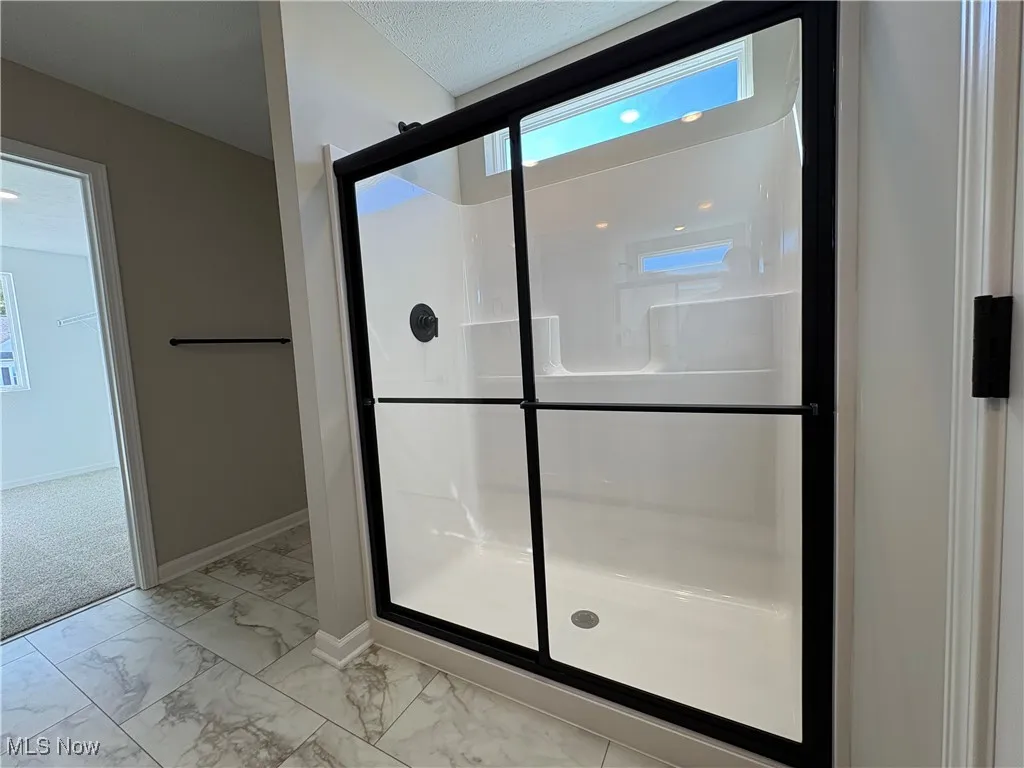 Full bathroom with light marble finish floors, a stall shower, and a textured ceiling