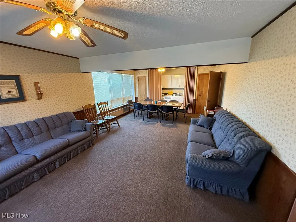 Living area with wallpapered walls, a textured ceiling, a ceiling fan, carpet, and ornamental molding