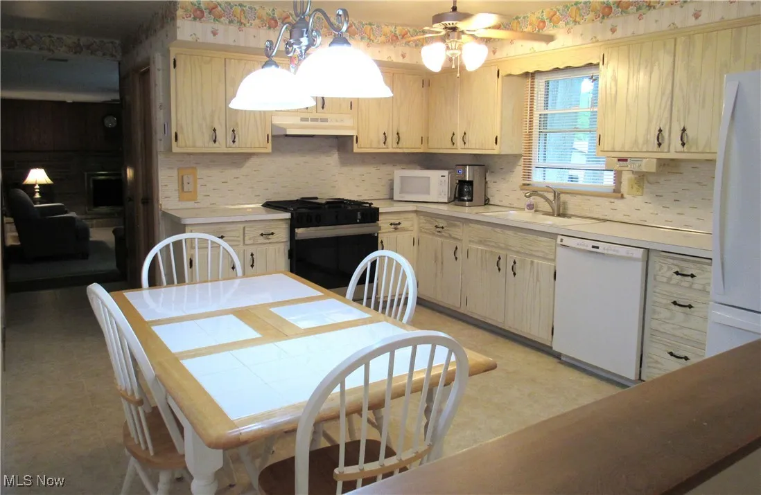Kitchen with light countertops, white appliances, decorative light fixtures, under cabinet range hood, and a ceiling fan